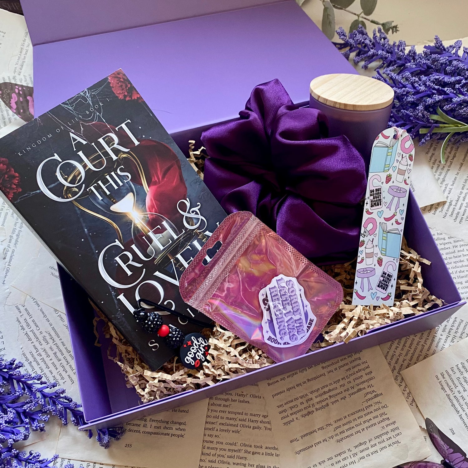purple monthly book subscription box featuring a book a court this cruel and lovely by stacia stark, a handmade candle, smutty and spicy themed bookmark fantasy stickers and a purple satin scrunchie