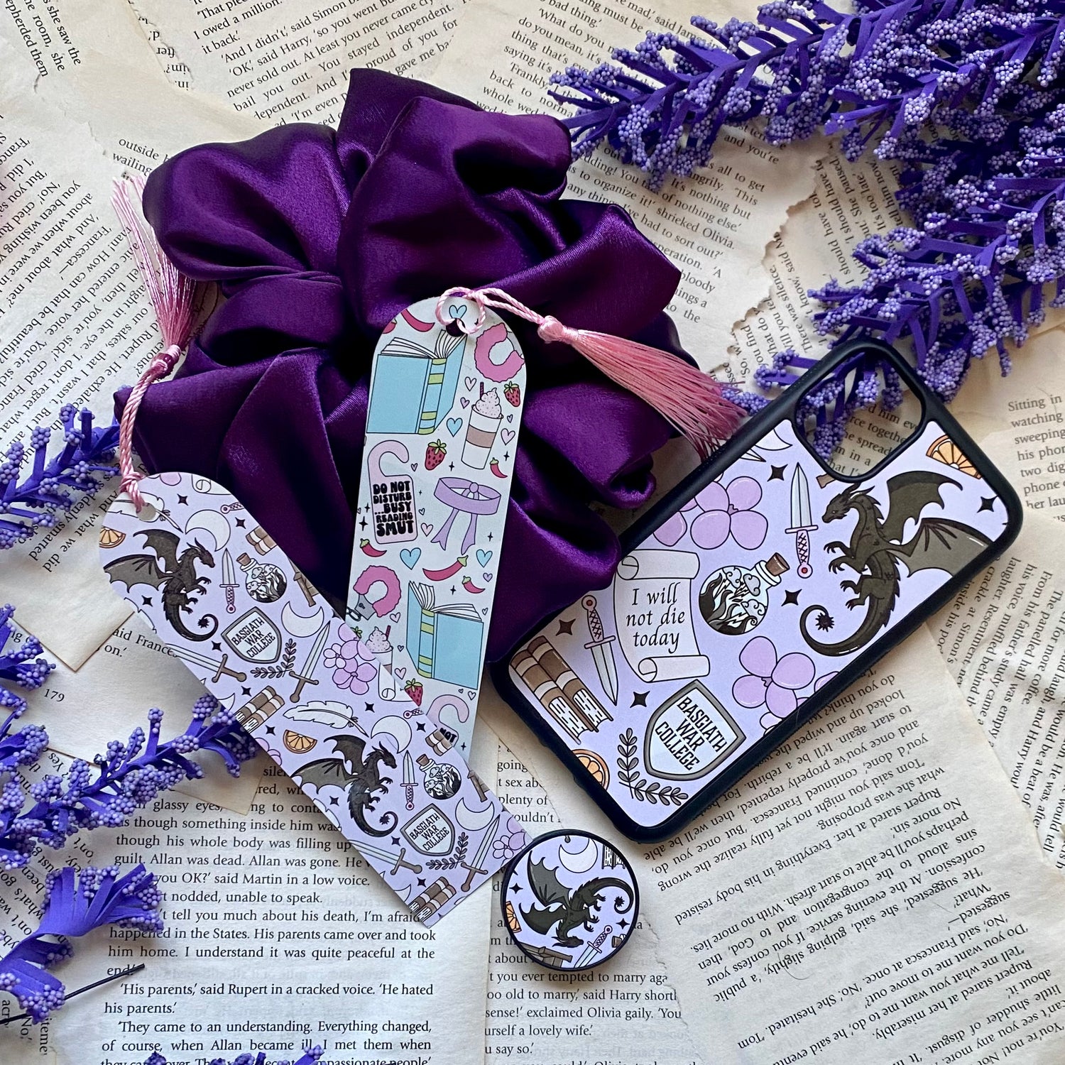 flat lay of two handmade bookmarks, a dragon-themed phone case, satin scrunchie and pop socket with spicy romance book design